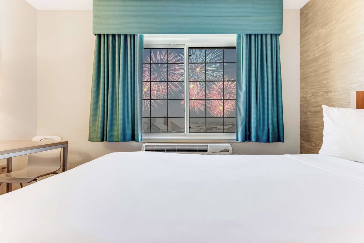 A hotel room with a bed, a table, and a window with curtains.