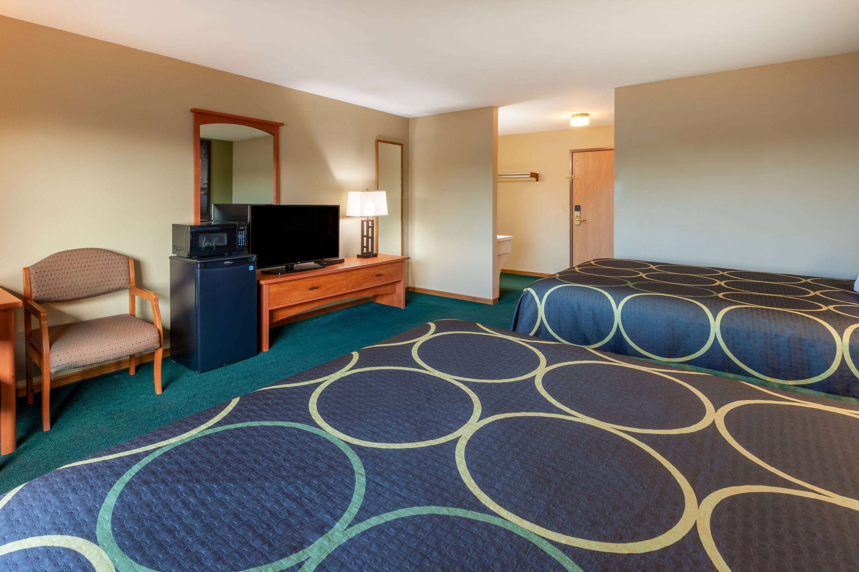 A hotel room with two beds, a desk with a television, a chair, and a small refrigerator.