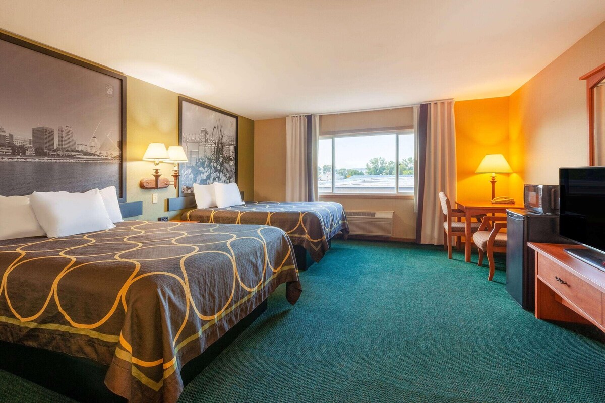 A hotel room with two beds, a desk with a television, and a window with curtains.