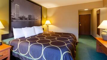 A hotel room with a large bed, two bedside lamps, a nightstand, a wooden dresser, and a door leading to another room.