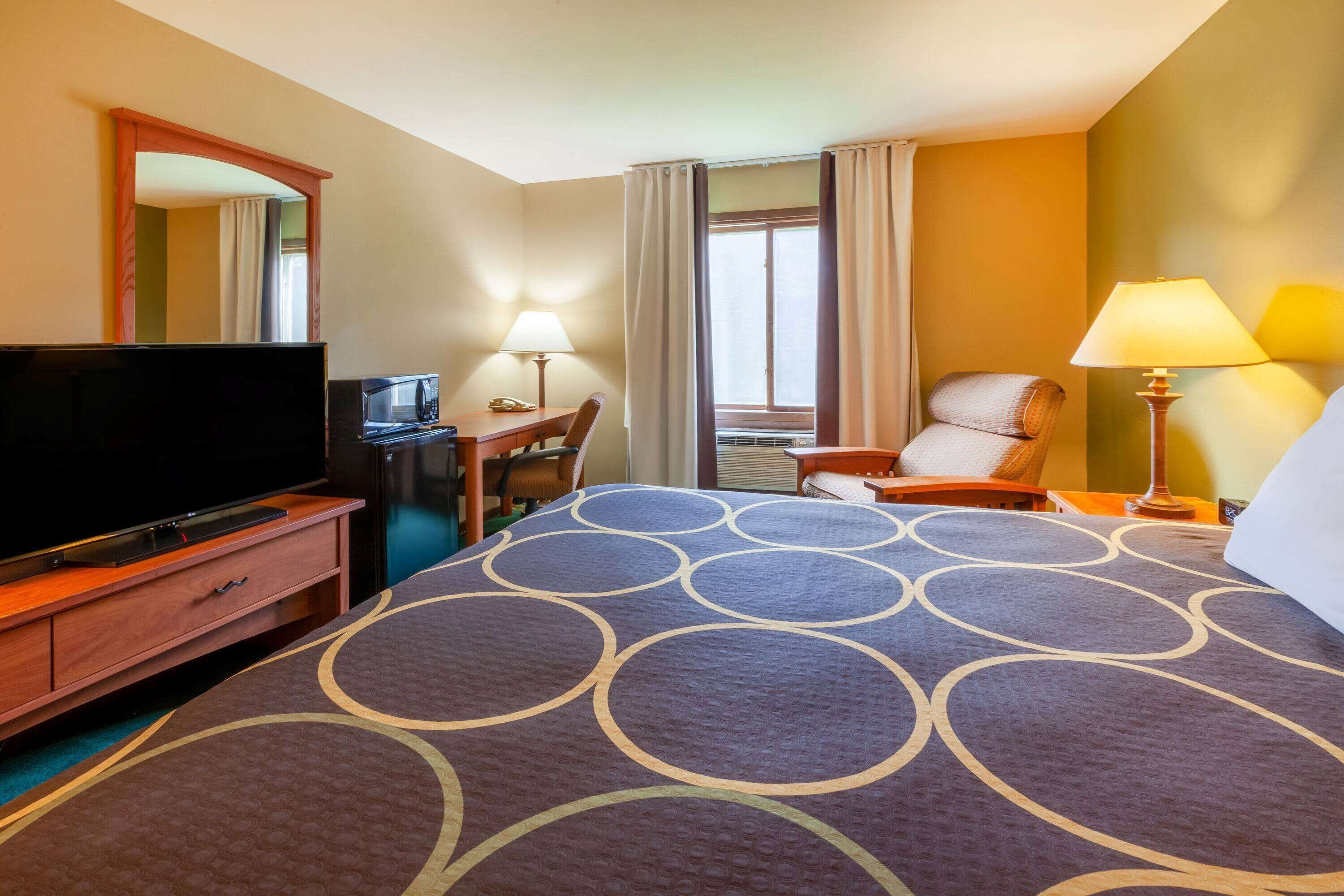 Una habitación de hotel con una cama grande, televisor, escritorio con lámpara y una silla.