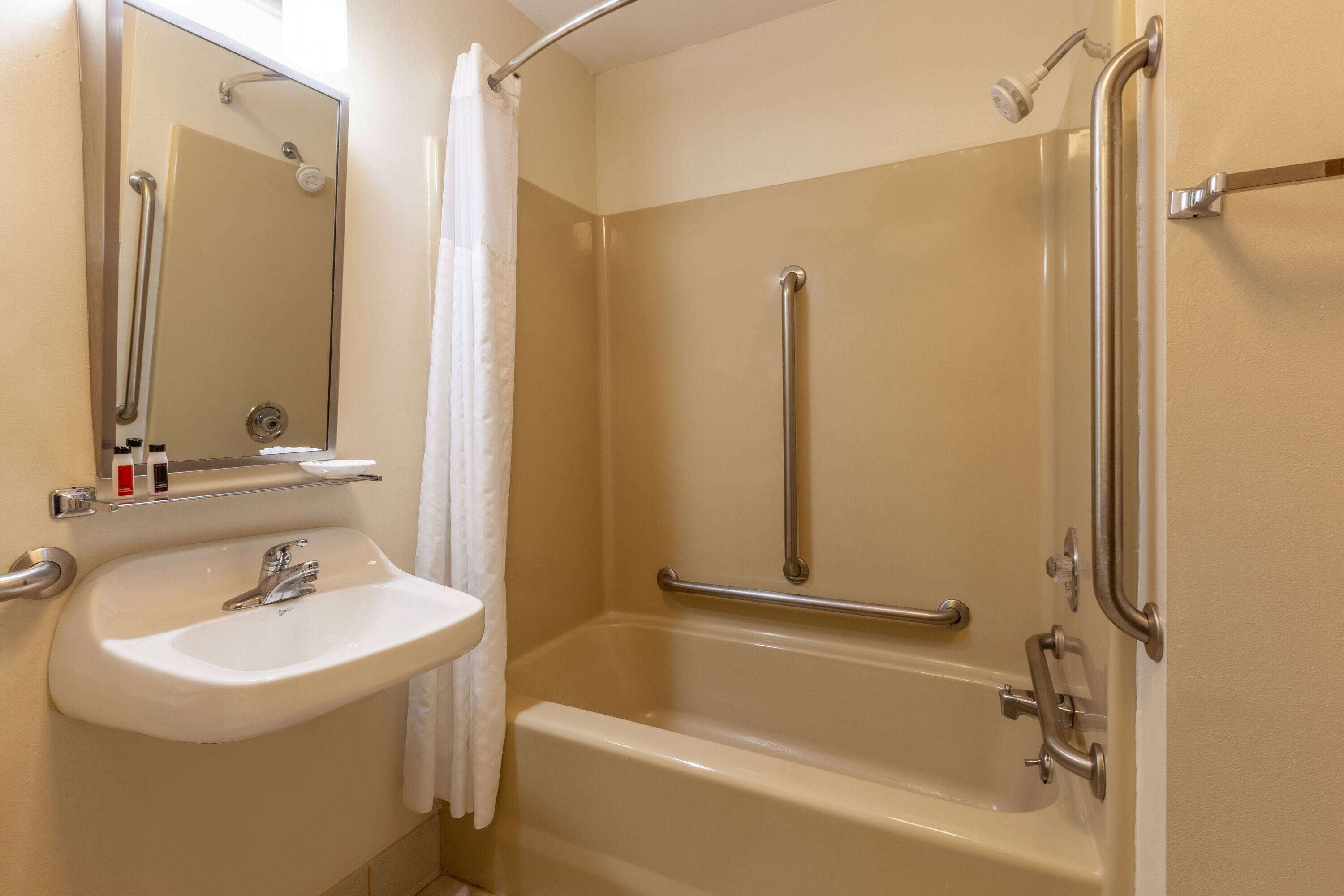 A bathroom with a sink, mirror, shower, and grab bars.