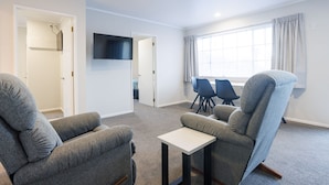 A modern living room with grey sofas, a small white table, and a TV mounted on the wall. - Bk's Pohutukawa Lodge (Whangarei)