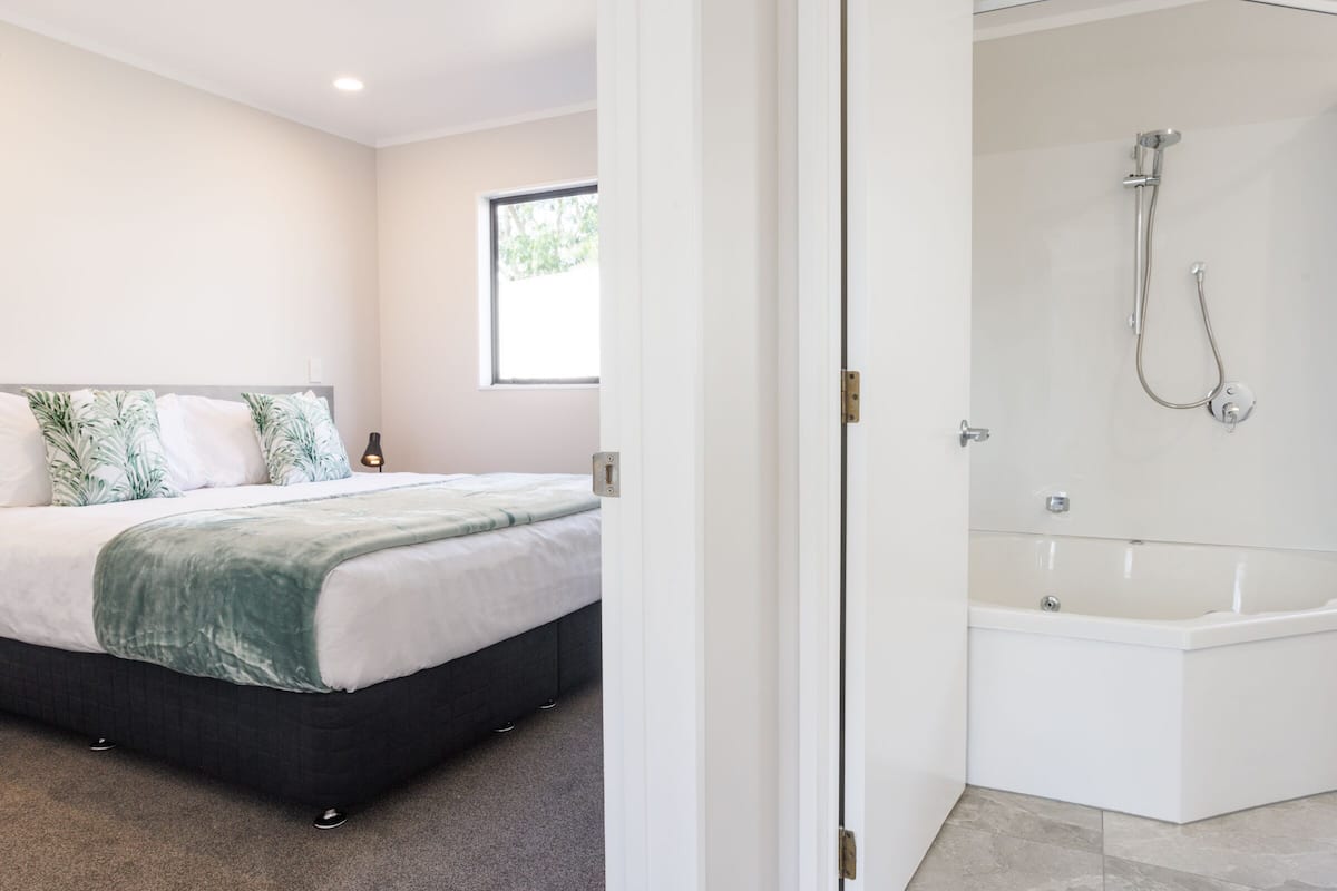 Un dormitorio moderno con una cama grande, una ventana y un espacio de ducha con bañera.