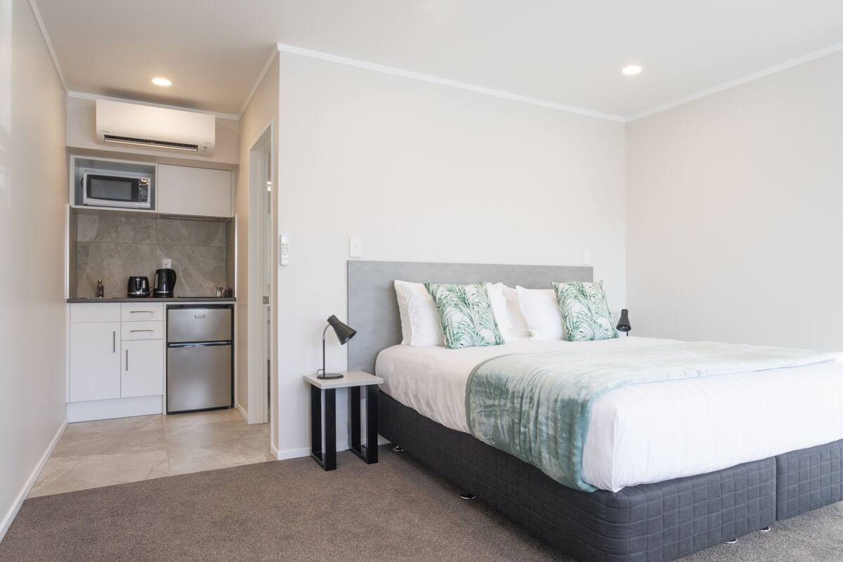 Un dormitorio con cama, mesita de noche y una pequeña kitchenette con microondas y refrigerador.