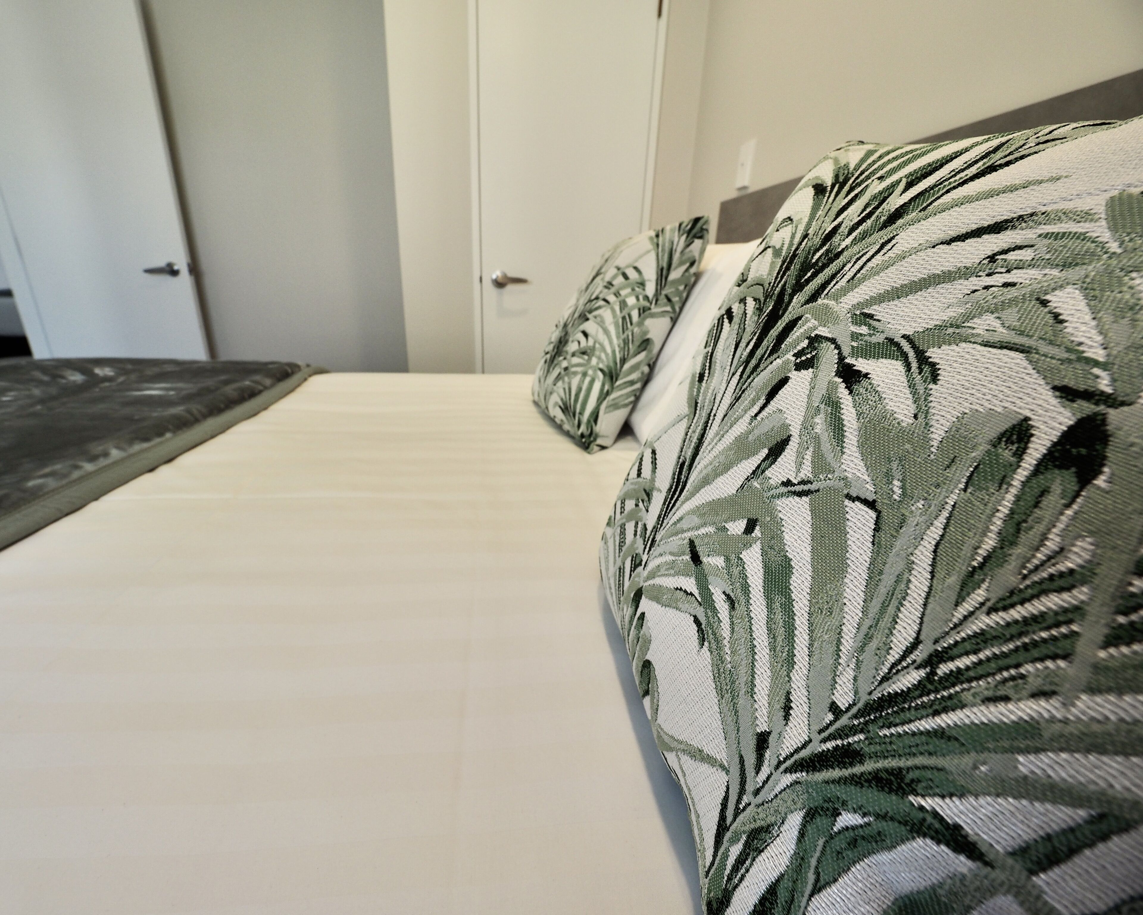 A bed with a white mattress and a pillow with a leaf pattern.