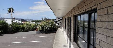 A covered walkway with a parking lot, a brick building, and a clear sky.