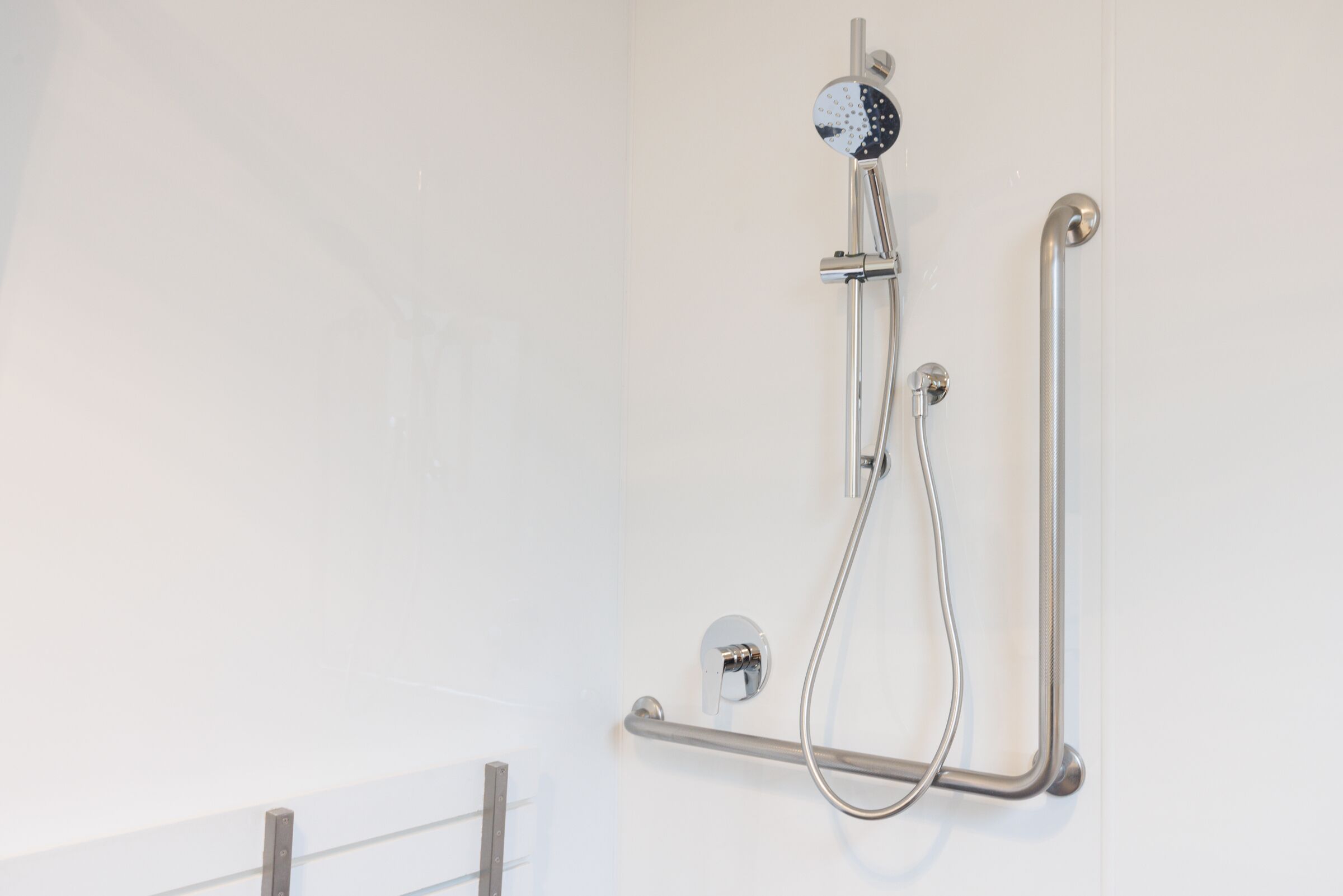 A bathroom with a shower, grab bars, and a handrail.