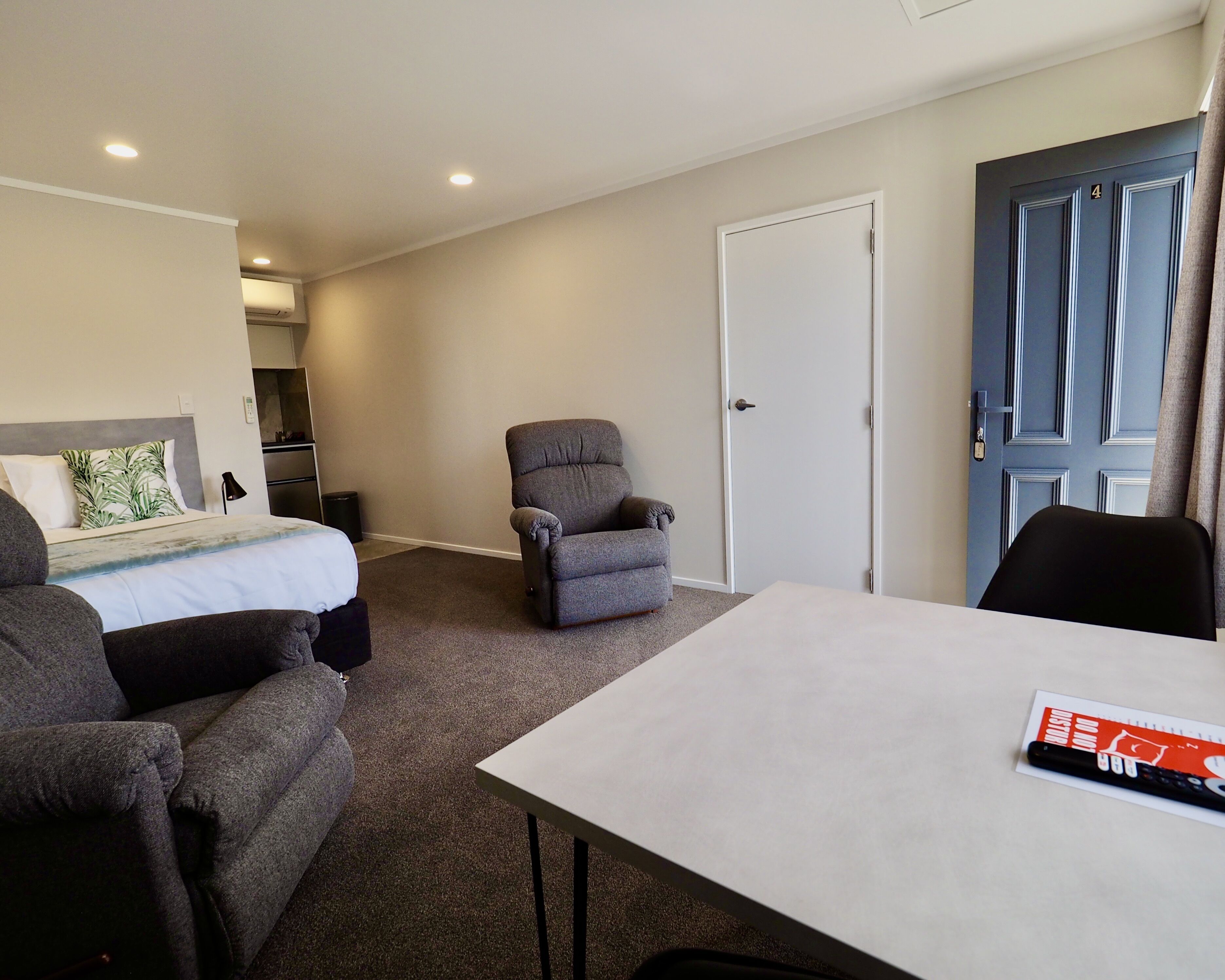 Una habitación de hotel con una cama, un sillón gris, una mesa y una puerta.