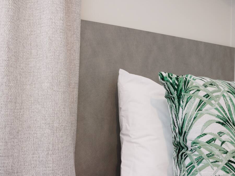 A bed with a grey headboard, a white pillow, and a green patterned pillow.