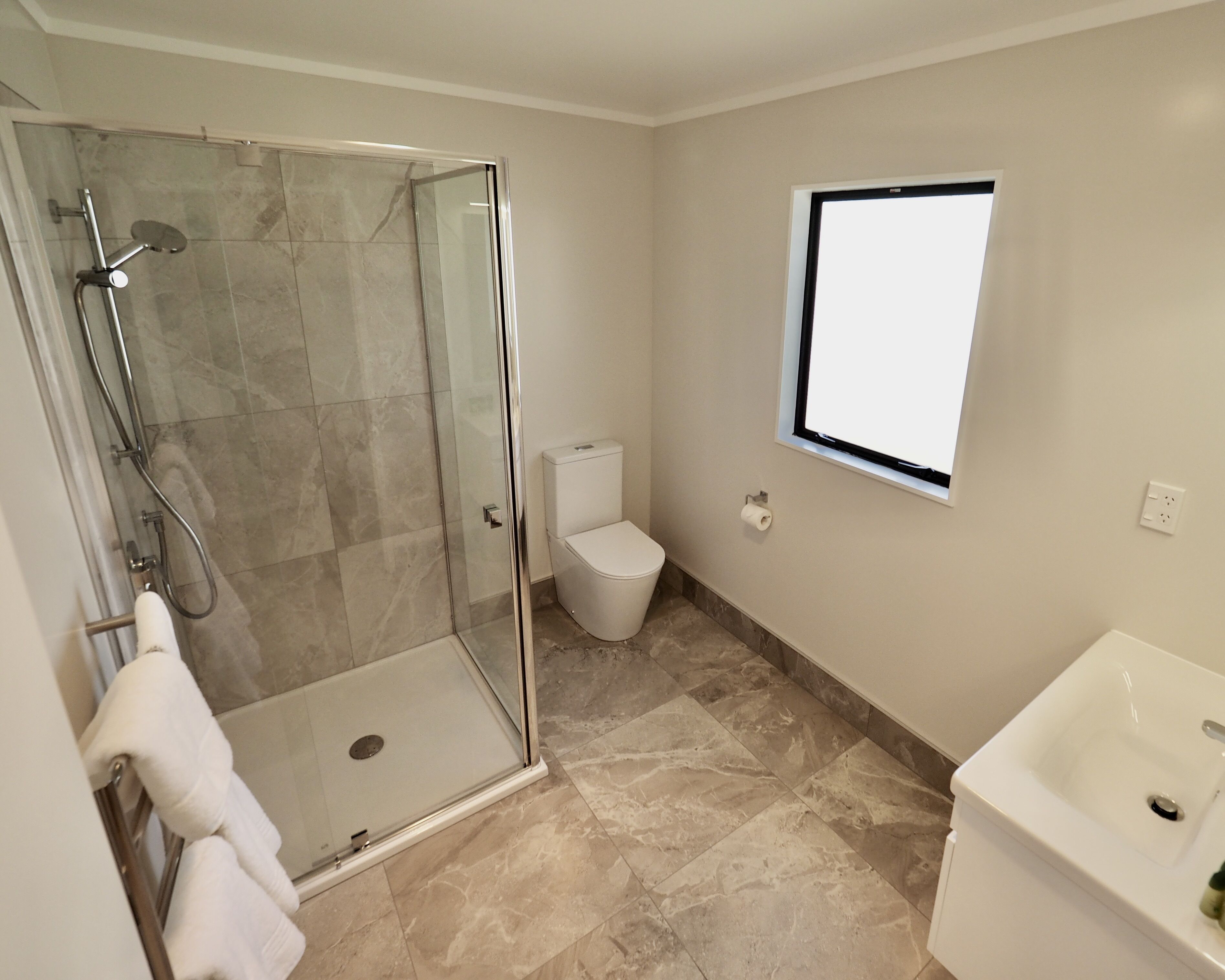 A bathroom with a glass-enclosed shower, a toilet, and a sink.