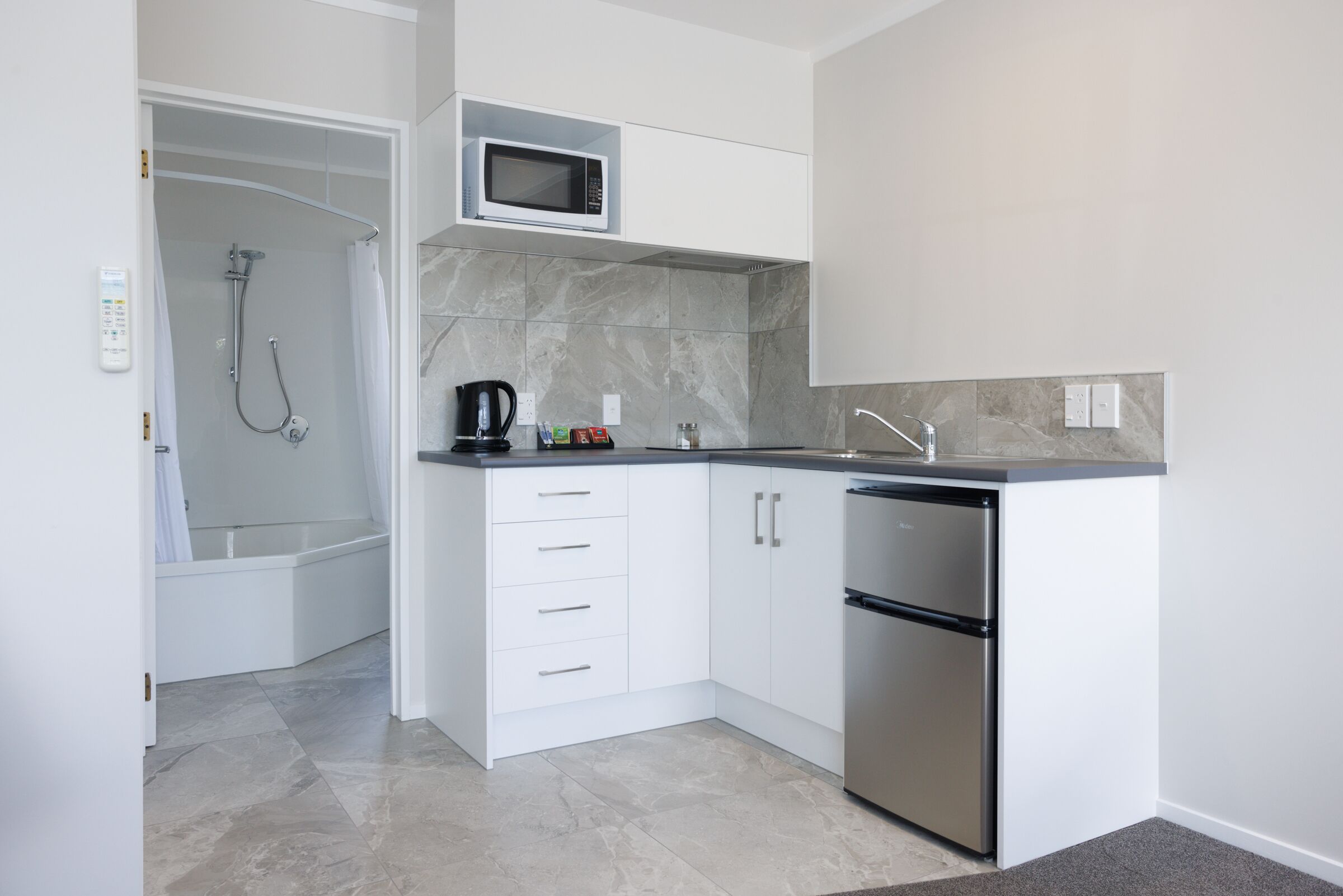 A compact kitchen with a built-in microwave, a dishwasher, and a shower area.