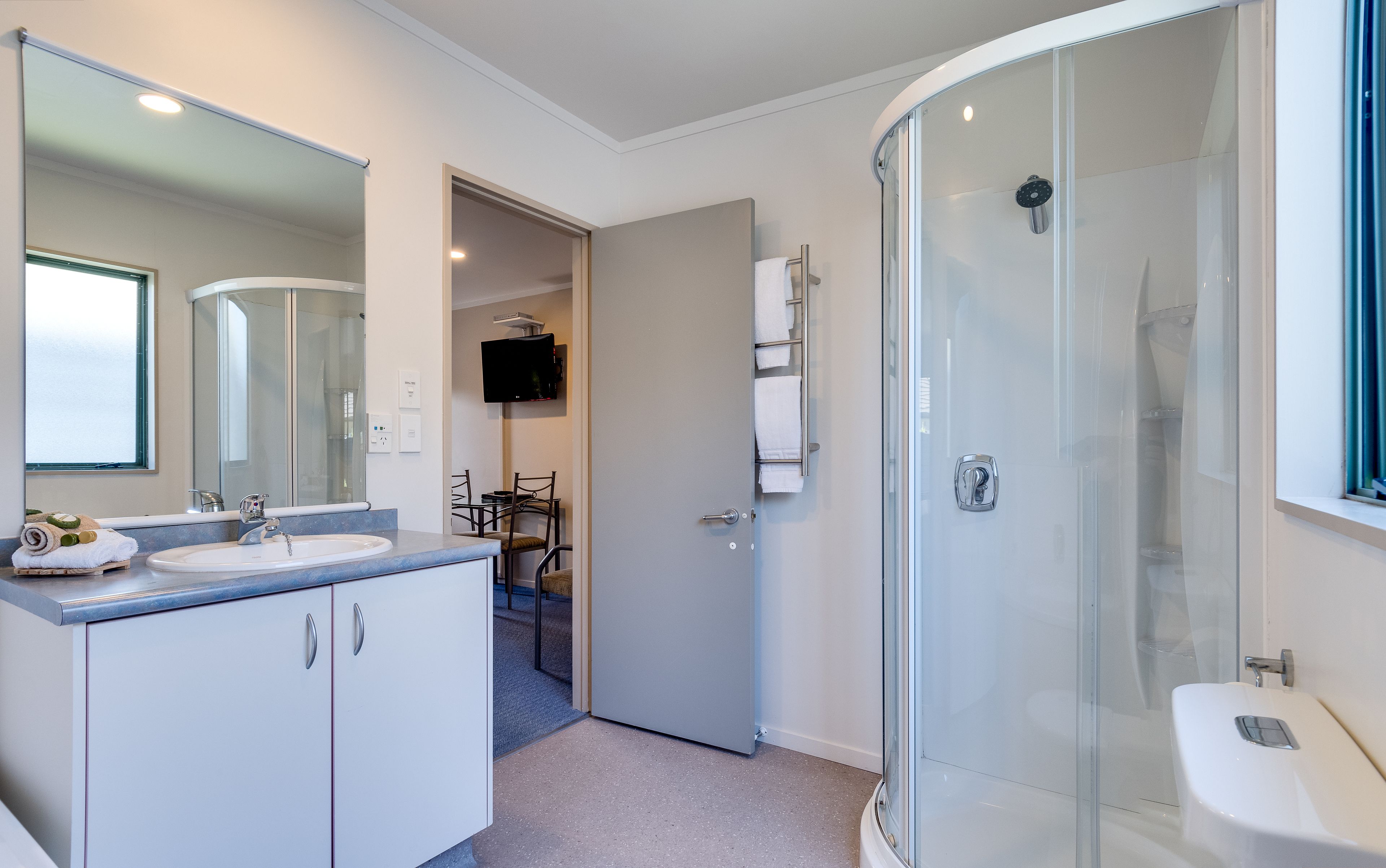 Een moderne badkamer met een douchecabine van glas, een wastafel met twee kommen en een flatscreen televisie aan de wand.