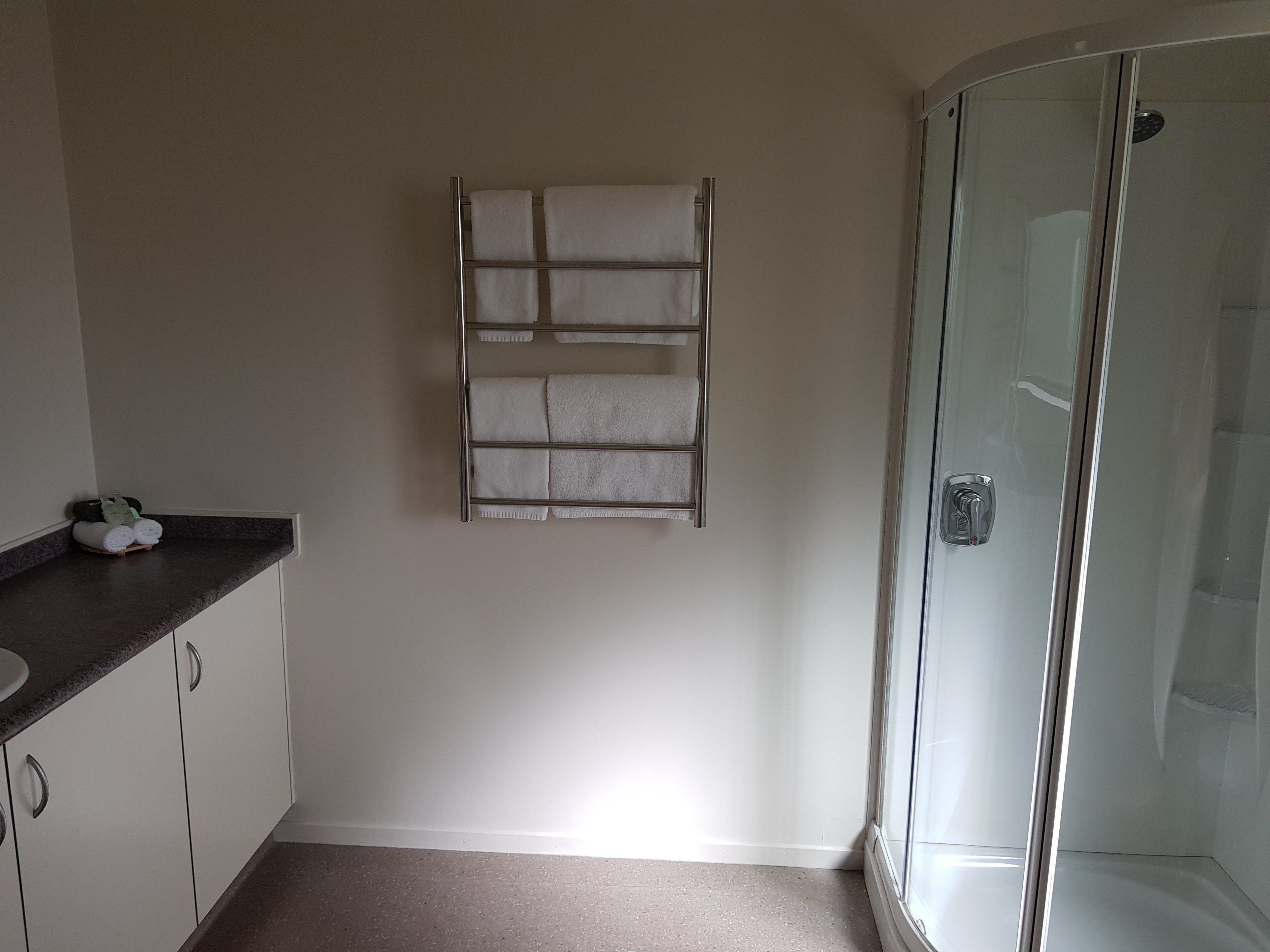 A bathroom with a glass shower enclosure, a towel rack with folded towels, and a dark countertop with a sink.