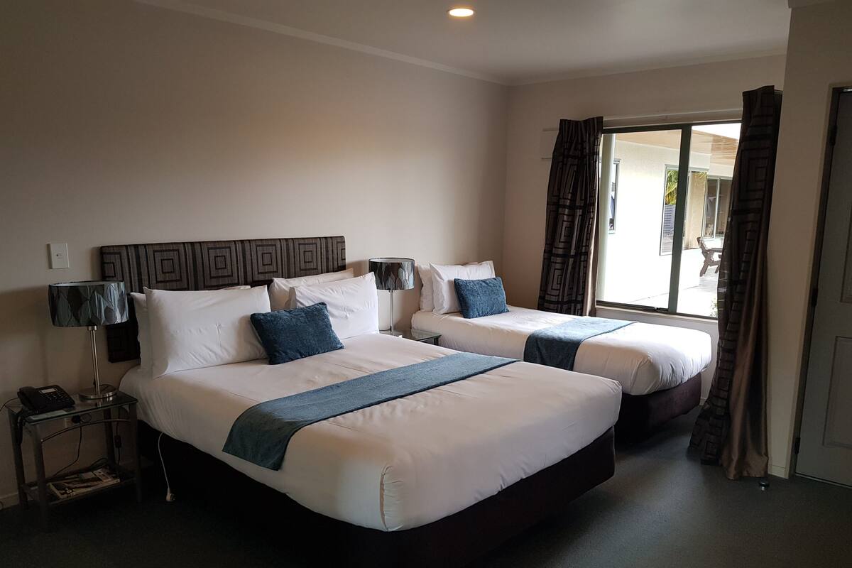 A hotel room with two beds, a nightstand with a phone, and a window with curtains.