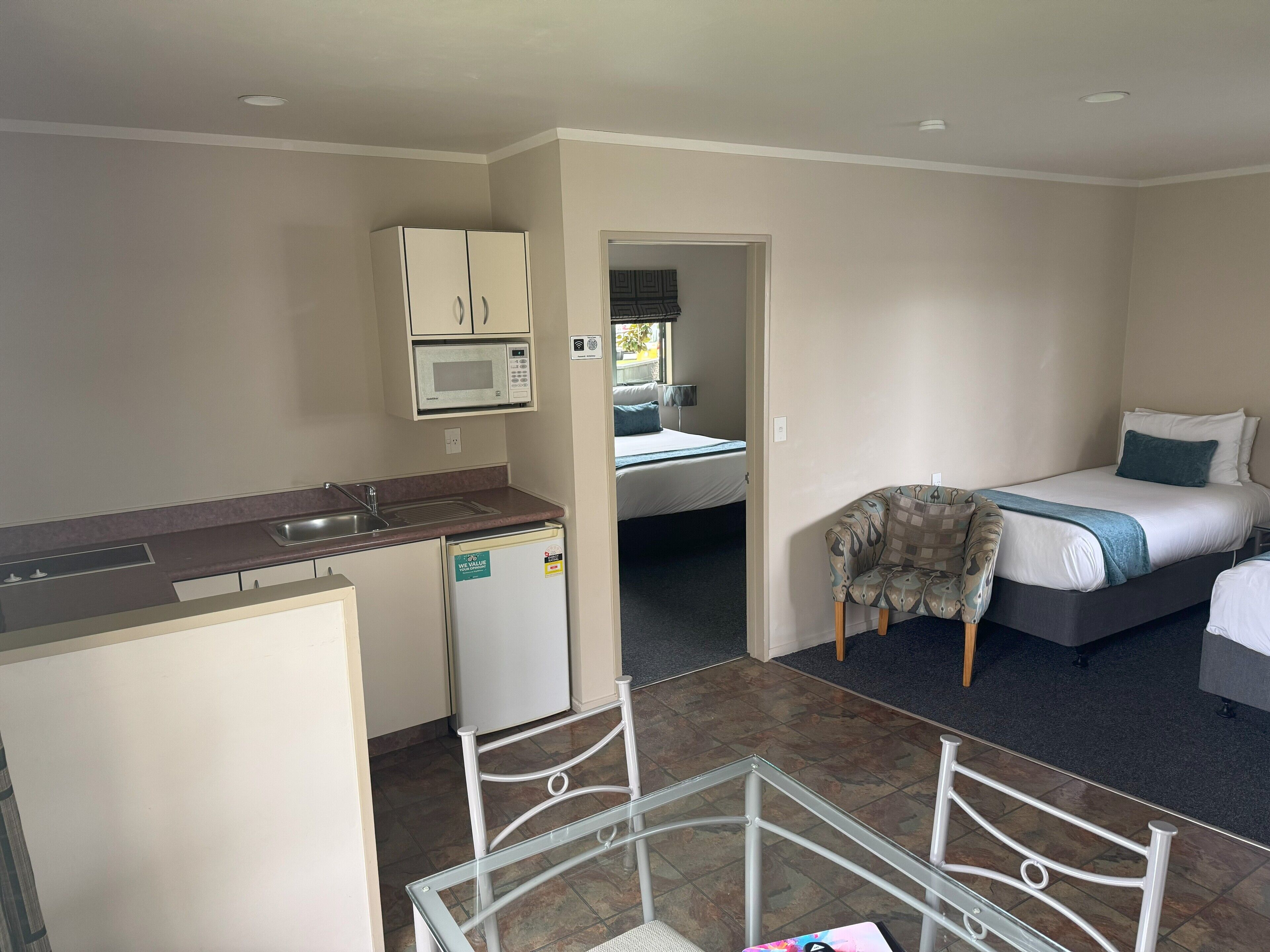 A compact hotel room with a kitchenette, a bed, and a small seating area.