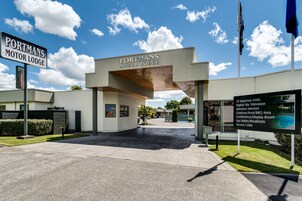 Exterior do Portmans Motor Lodge, com céu claro e placa listando comodidades como 20 unidades espaçosas, televisão digital e piscina ao ar livre.
