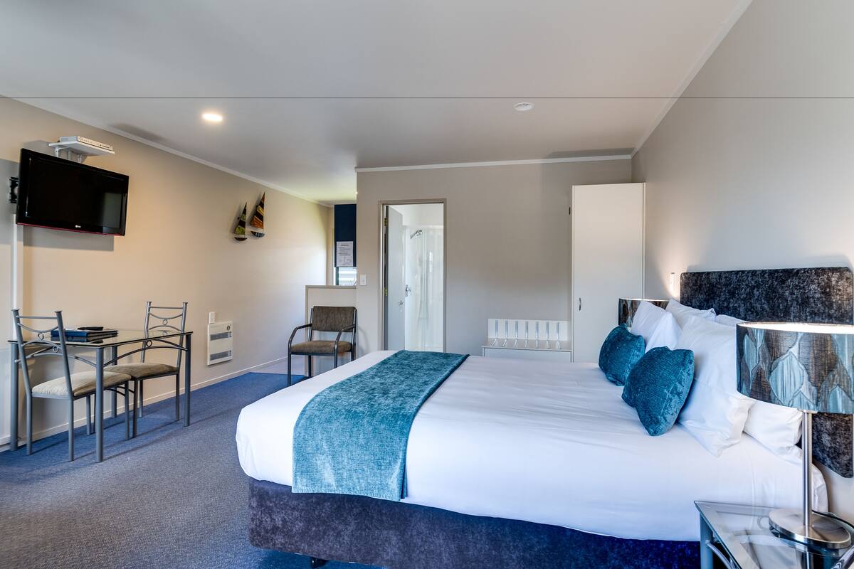 A hotel room with a large bed, a desk with chairs, a television, and a bathroom door.