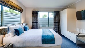 A hotel room with a large bed, a desk with a lamp, a wardrobe, and a TV mounted on the wall. - Portmans Motor Lodge (Hastings)