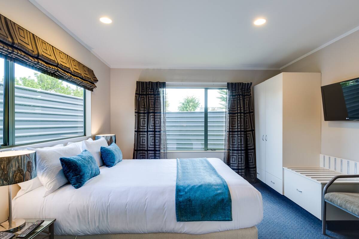 A hotel room with a large bed, a desk with a lamp, a wardrobe, and a TV mounted on the wall.