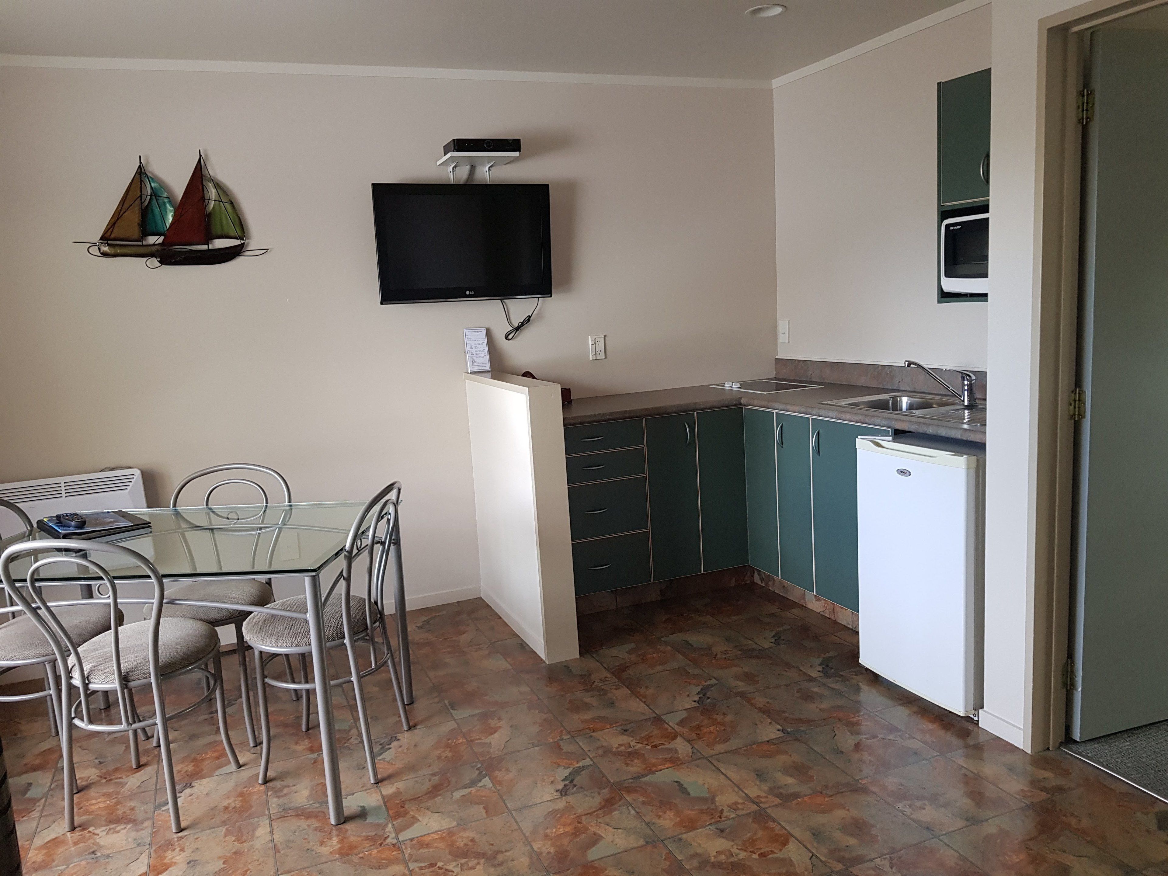 A compact kitchen with a dining area, a flat-screen TV mounted above the counter, and a microwave above the sink.