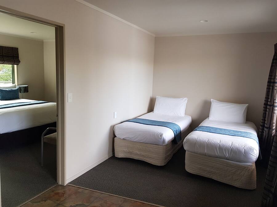 A hotel room with two single beds, a small desk, a chair, and a window with a view of greenery.