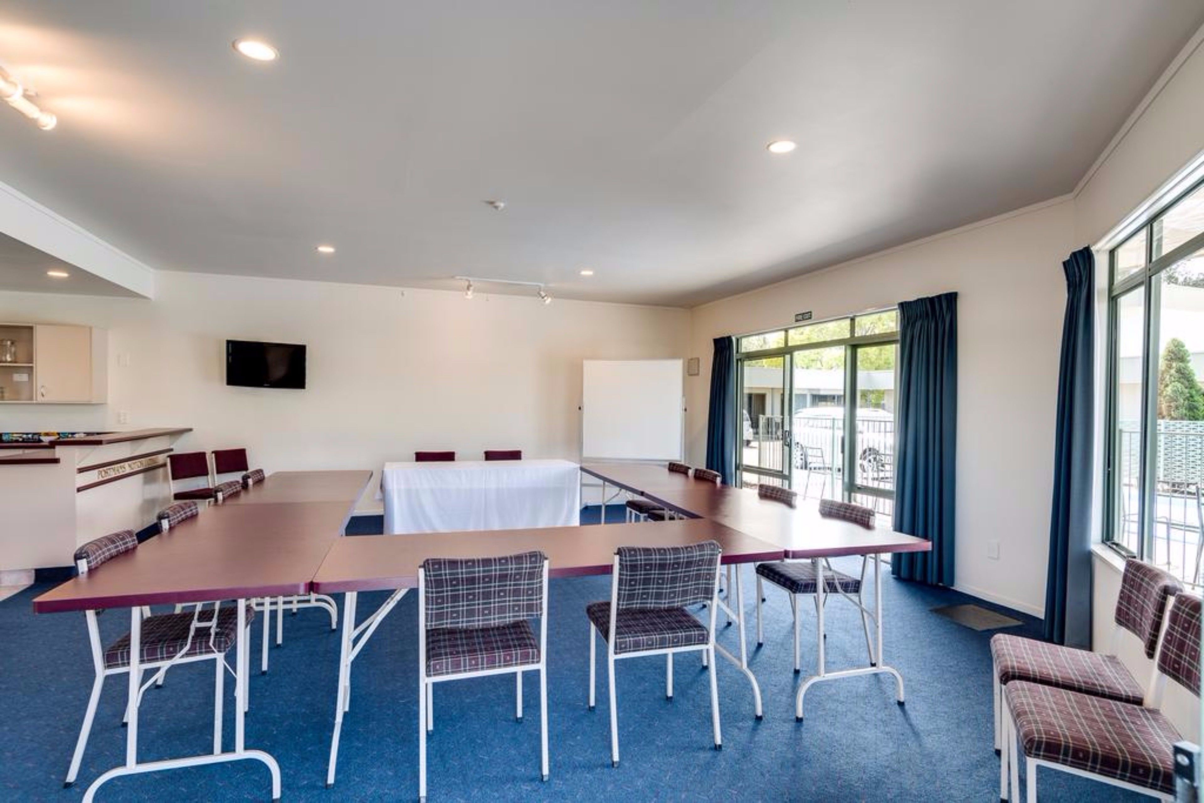 Uma sala de conferência com uma mesa comprida, várias cadeiras, um quadro branco e uma televisão na parede.