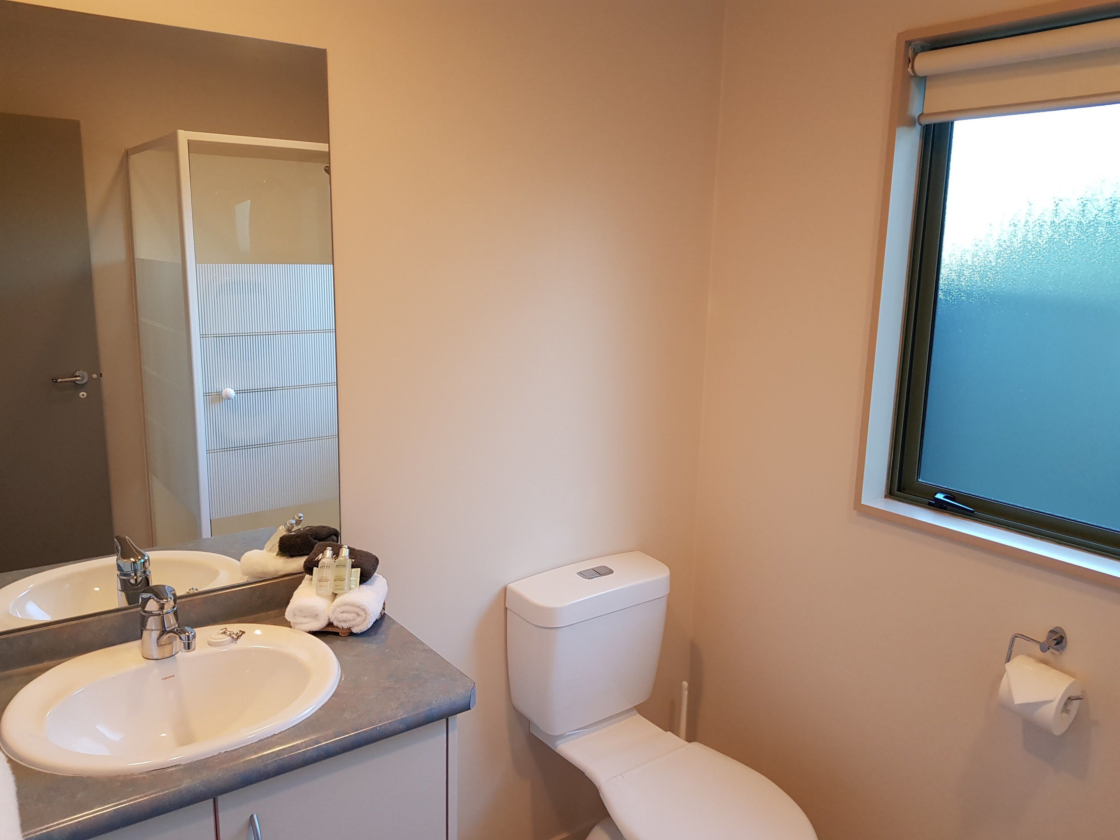 A bathroom with a double sink, a toilet, a window, and a towel rack.