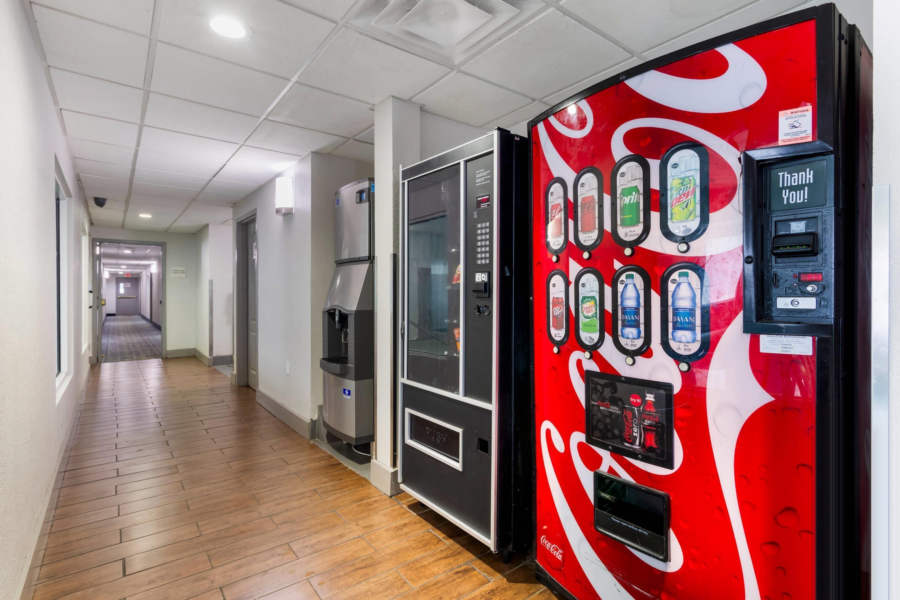 A hallway with a Coca-Cola branded vending machine, a water dispenser, and a refrigerator.
