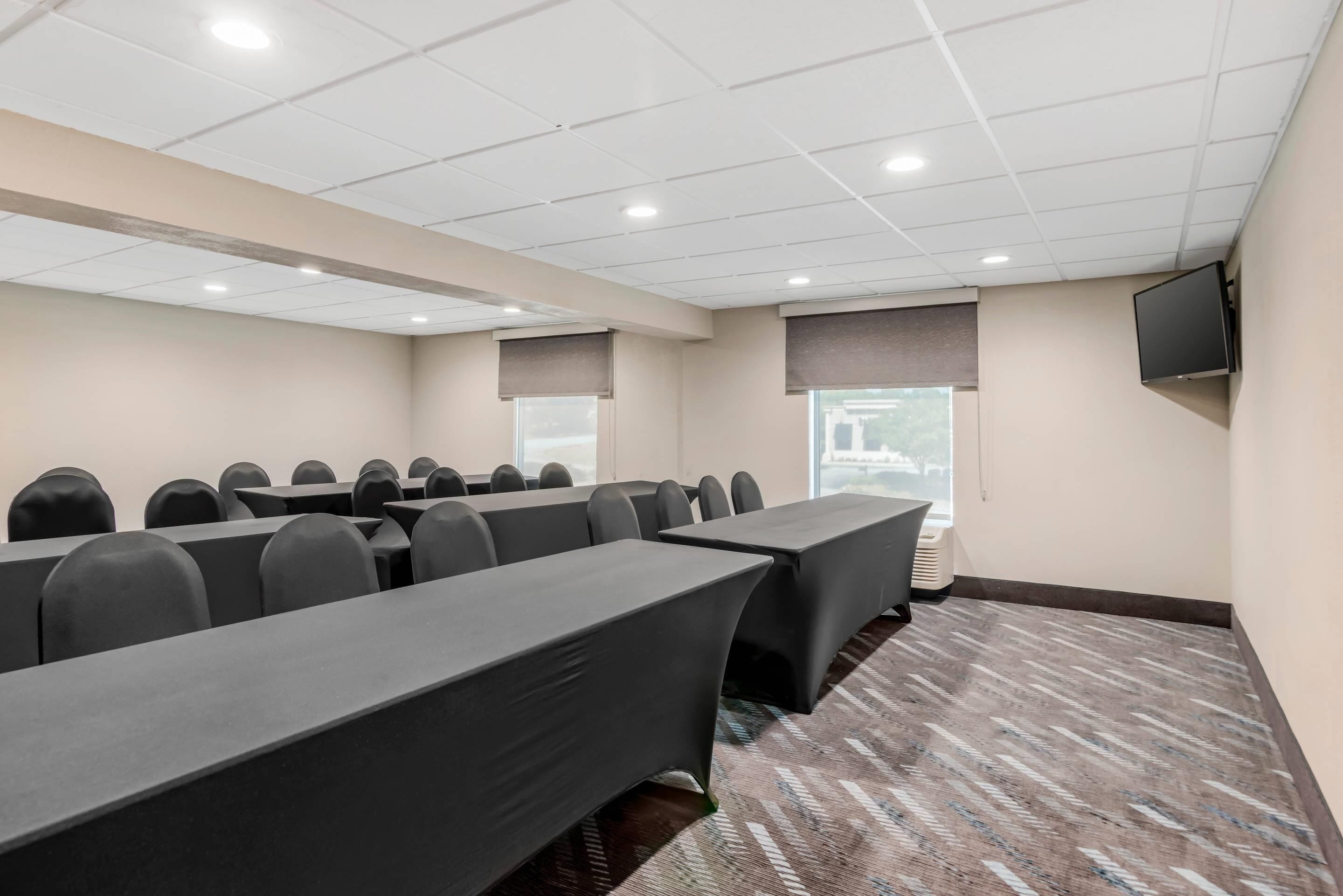 A conference room with long tables, chairs, and a flat-screen TV on the wall.
