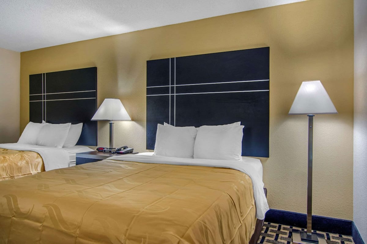 A hotel room with two beds, a nightstand, a lamp, and a large wall art piece.