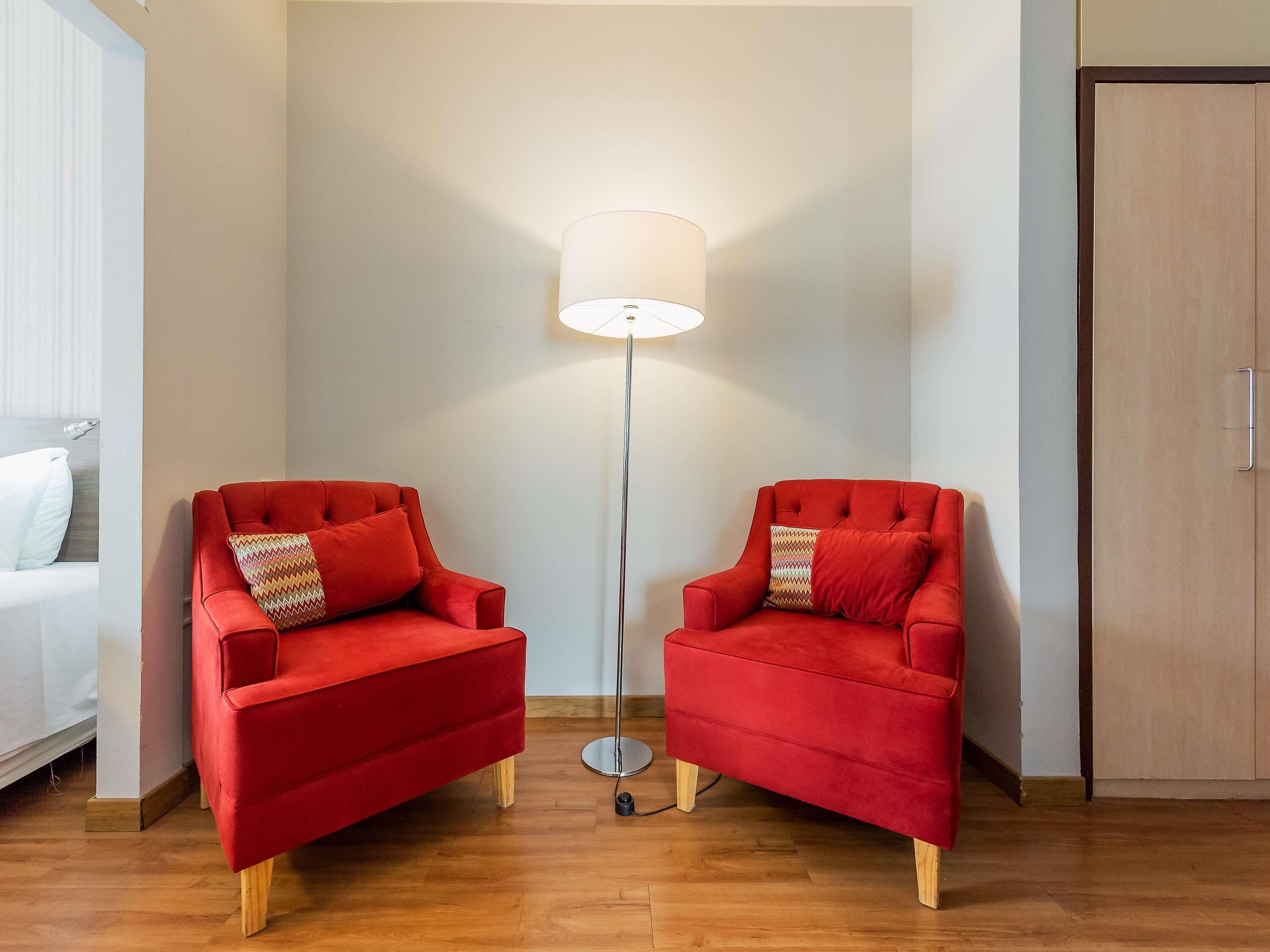 A room with two red armchairs, a floor lamp, and a wooden wardrobe.
