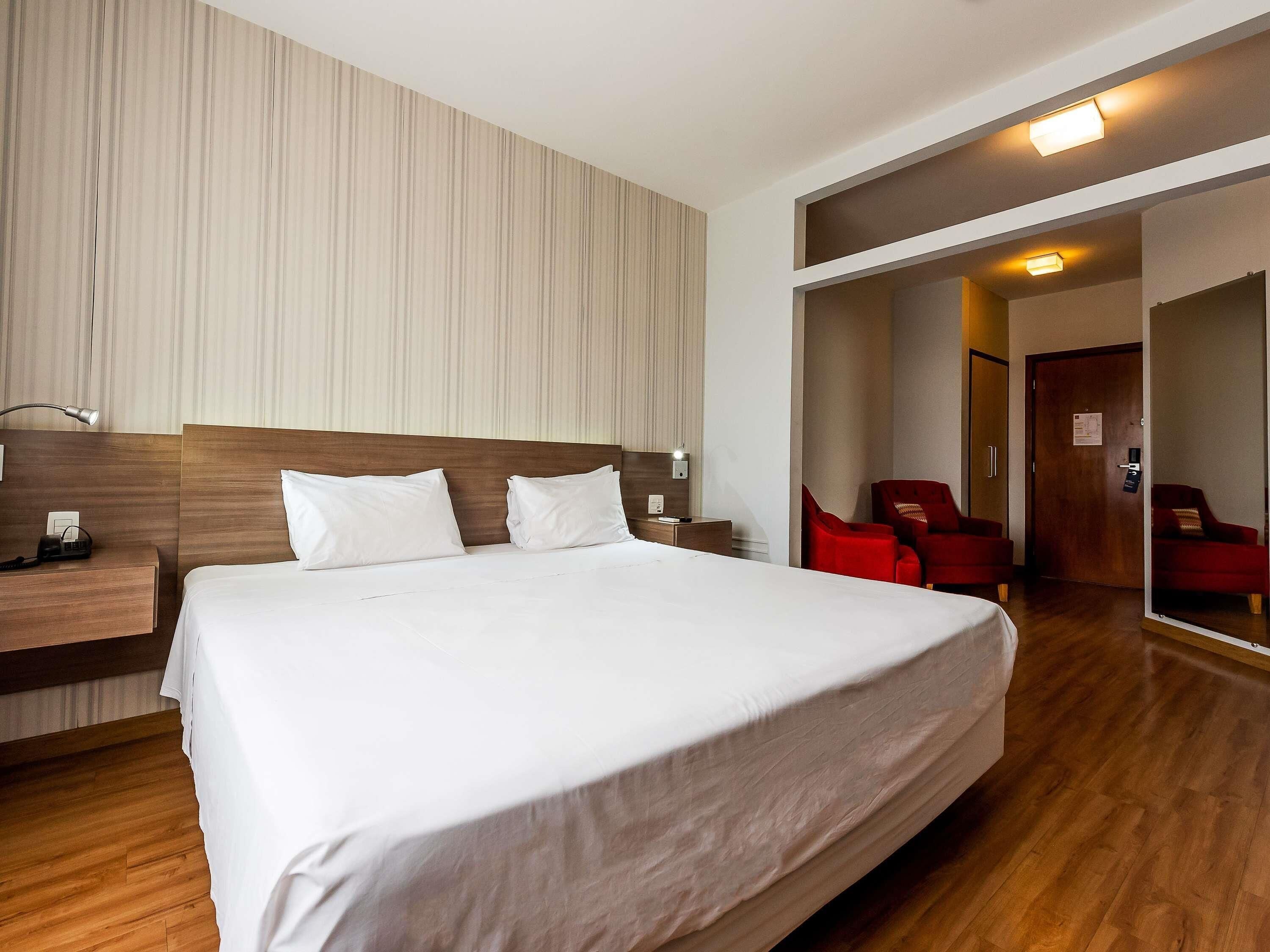 A hotel room with a large bed, a nightstand, a desk, a chair, and a mirror.