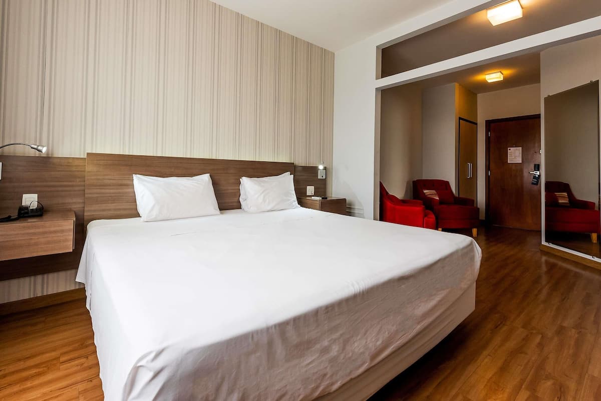 A hotel room with a large bed, a nightstand, a desk, a chair, and a mirror.