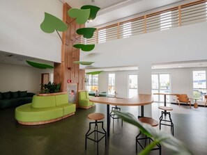 A modern interior with a curved green sofa, a wooden accent wall, and a central round table with stools. - ibis Styles Campinas Alphaville (Campinas)