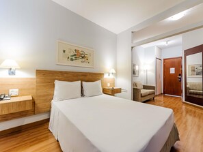Una habitación de hotel con una cama grande, lámparas de noche, un cabecero de madera, una mesita de noche, un teléfono y un cuadro en la pared.