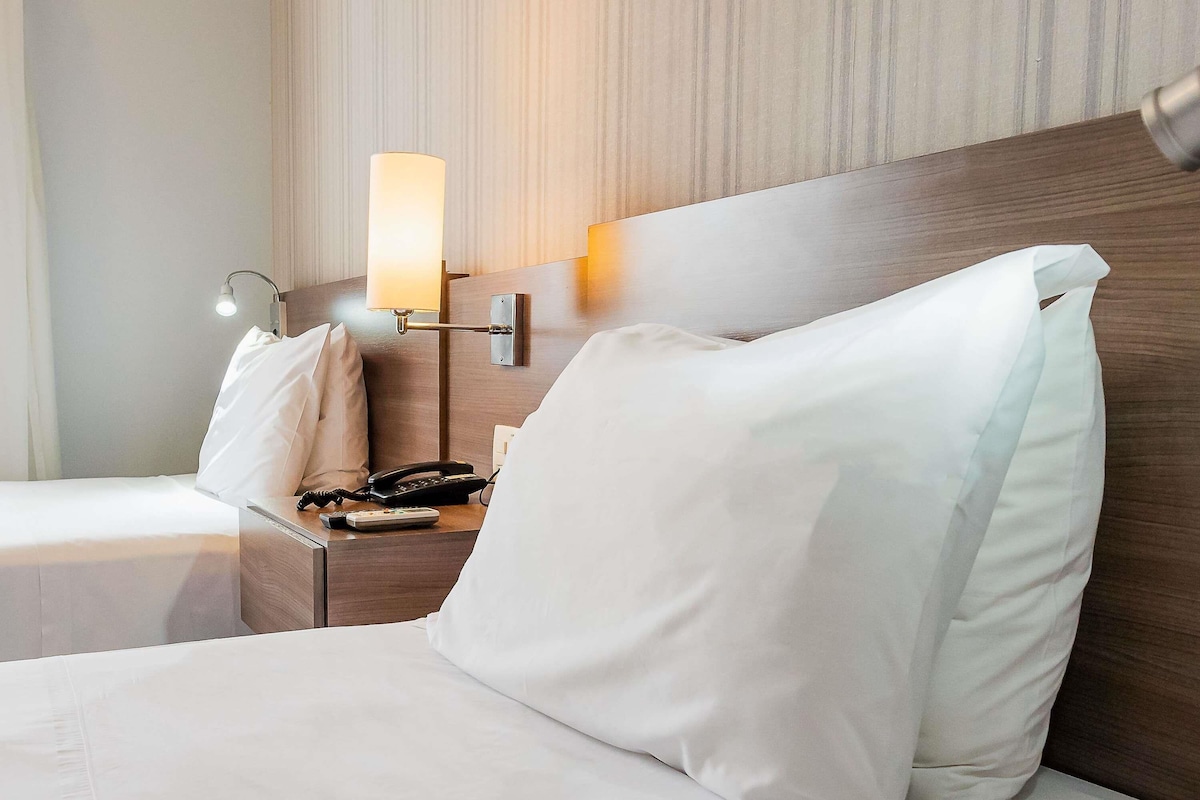 Una habitación de hotel con una cama bien hecha, una mesita de noche con una lámpara, un teléfono y un control remoto.