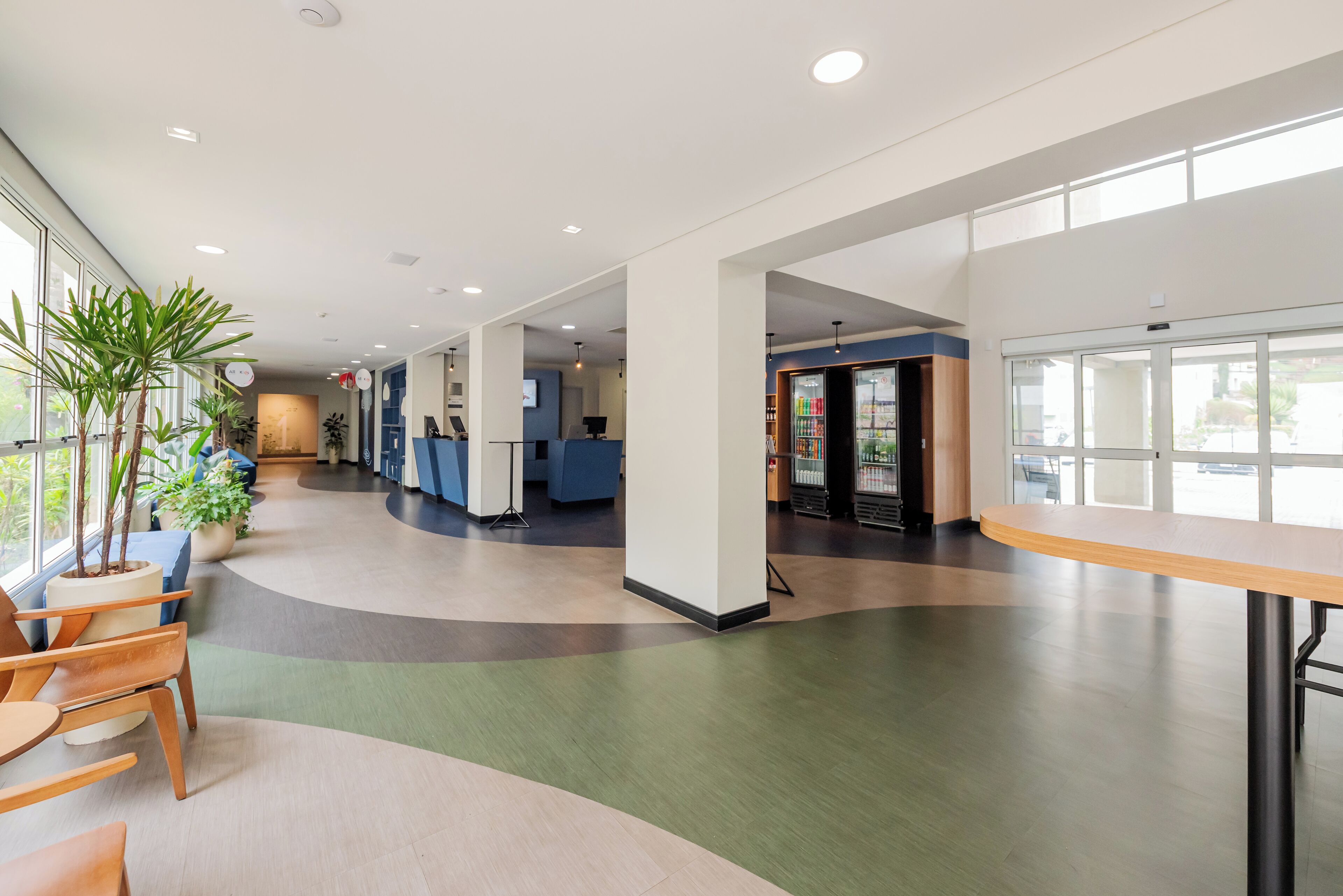 A spacious hallway with a curved ceiling, potted plants, and a reception area with a blue counter.