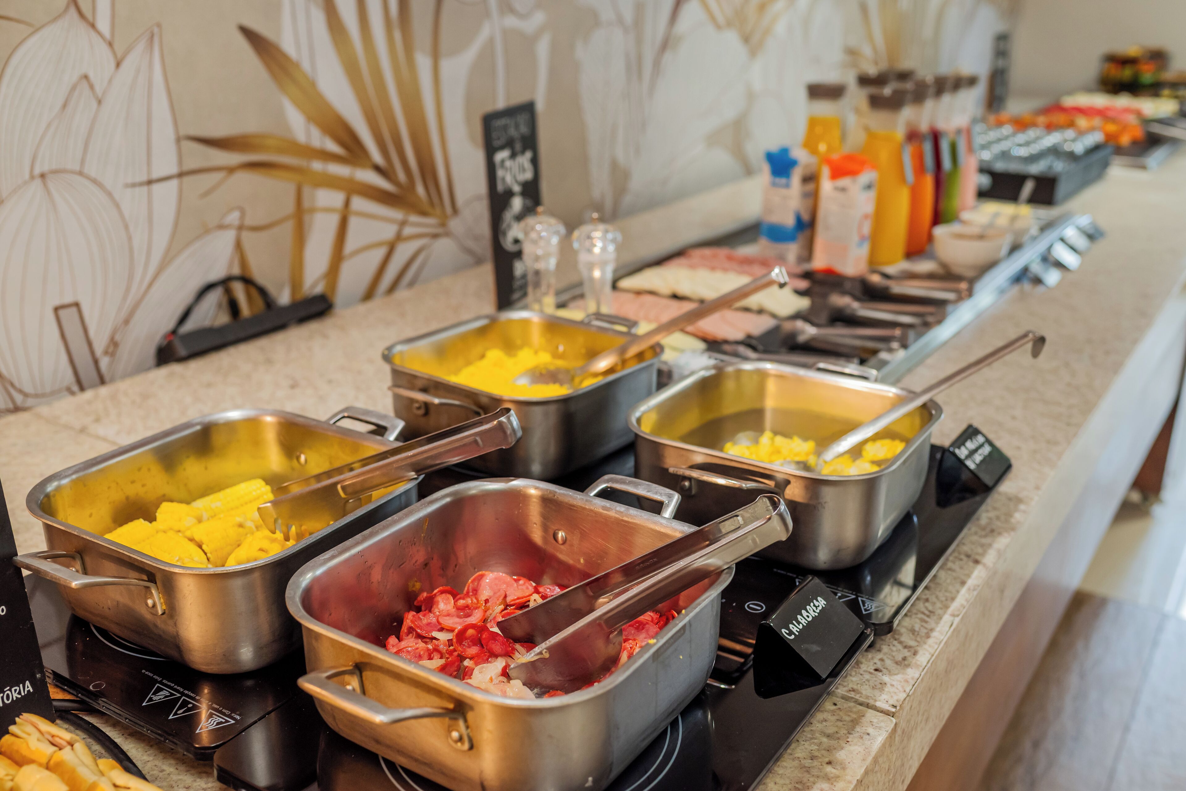 A buffet with various food items in metal containers, including yellow and red dishes, and condiments in the background.