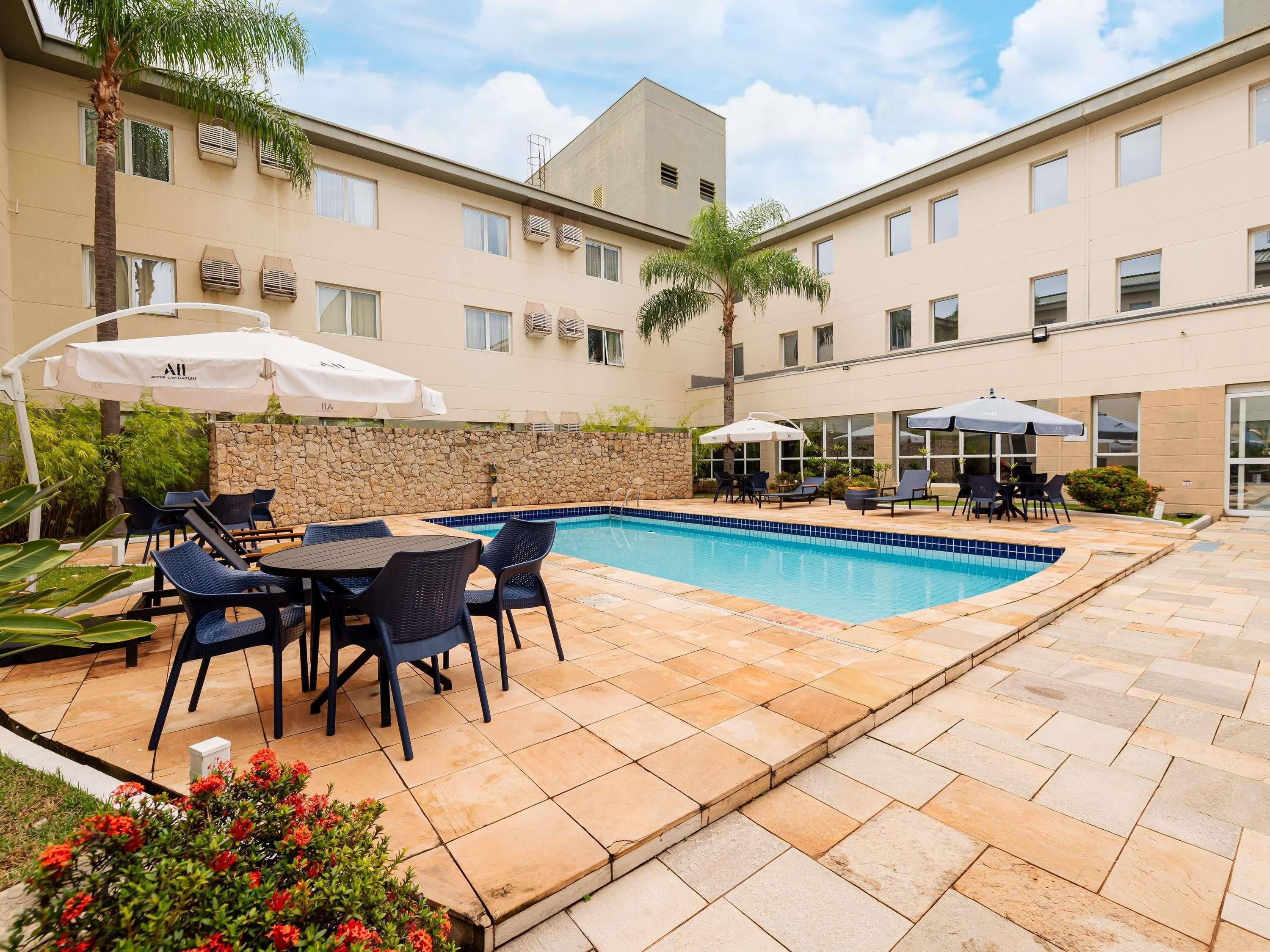 A poolside area with outdoor seating and umbrellas, a stone wall, and a building with multiple windows and air conditioning units.
