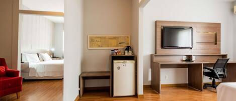 A hotel room with a bed, a desk with a TV, a small fridge, and a red chair.