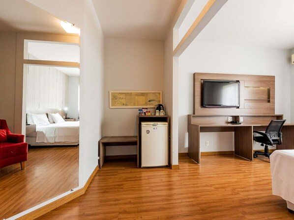 Habitación de hotel con cama, escritorio con televisor, un refrigerador pequeño y una silla roja.