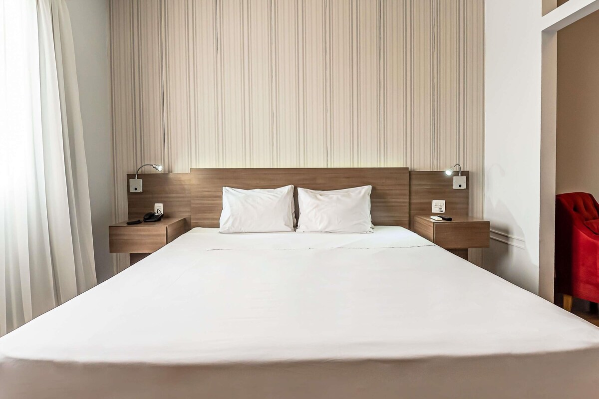 A modern hotel room with a large bed, two bedside tables, and a wooden headboard.