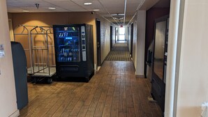 A hotel hallway with a vending machine, a metal rack, and a tiled floor. - St Clair Inn and Suites (St. Clairsville)