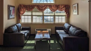 A room with two leather sofas, a small table, and a large window with blinds. - St Clair Inn and Suites (St. Clairsville)