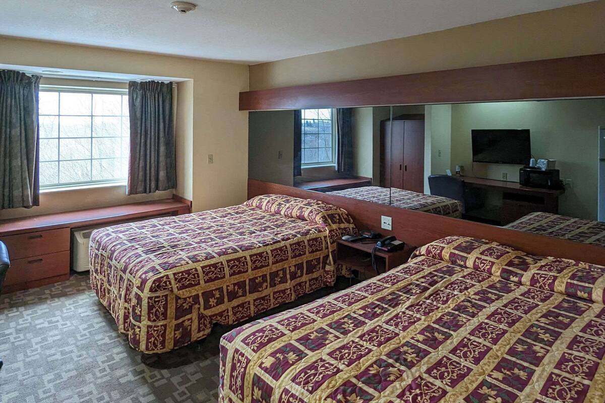 Habitación de hotel con dos camas, un escritorio, una silla, un televisor y un refrigerador.