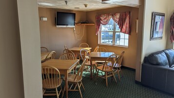 Un comedor con mesas y sillas de madera, un televisor de pantalla plana en la pared, una ventana con cortinas y un sofá.