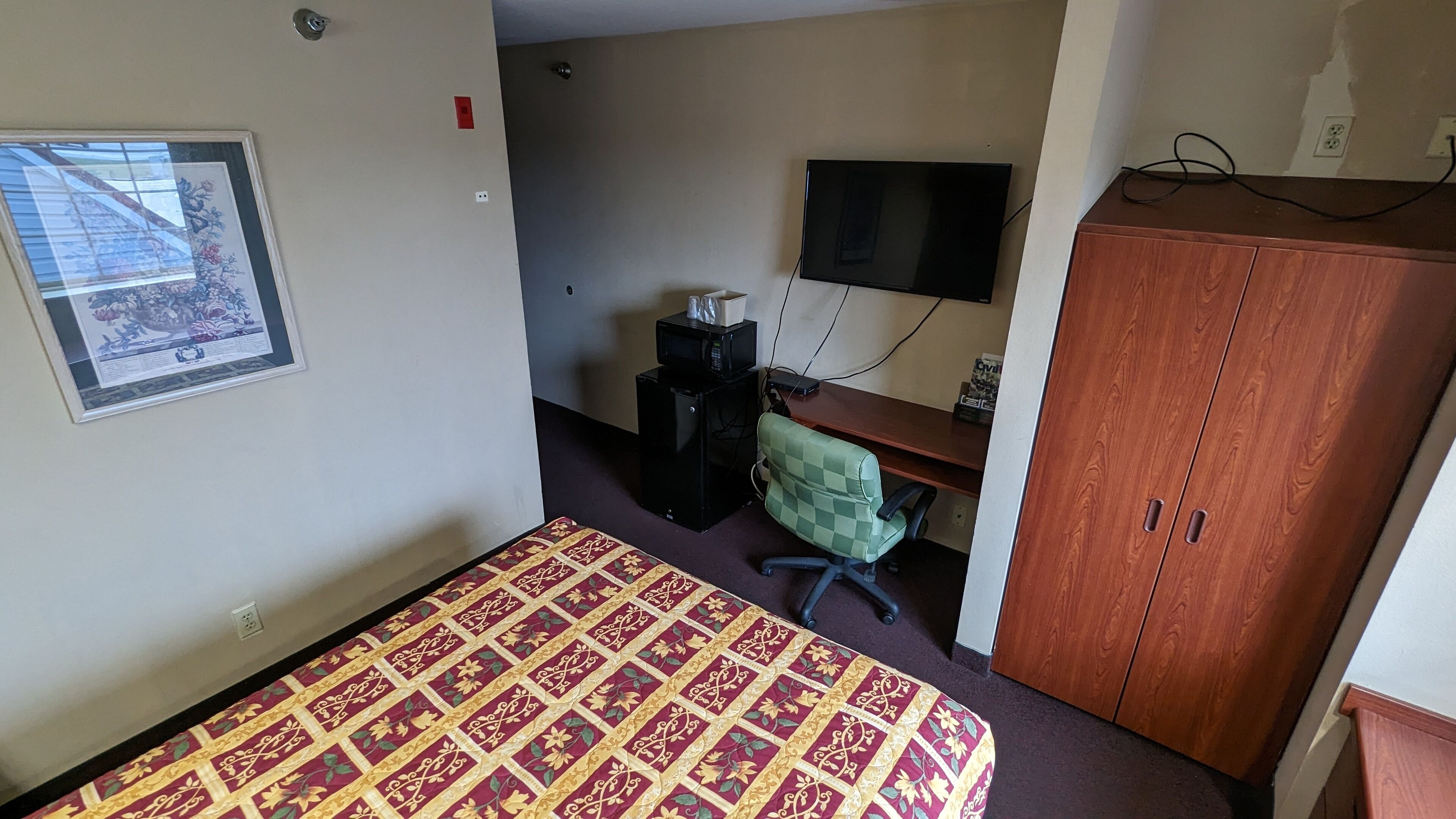 Een kleine kamer met een bed, een bureau, een televisie en een kledingkast.