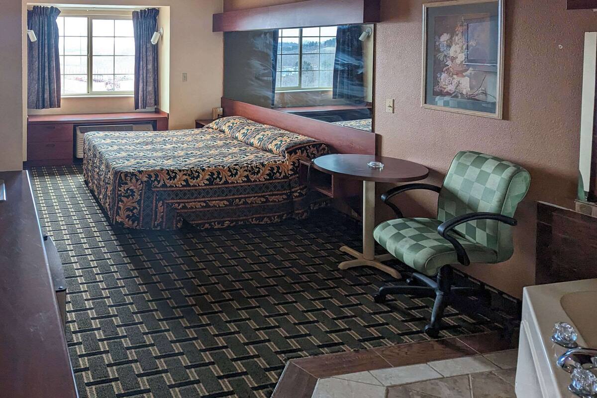 Habitación de hotel con cama, una mesita, una silla, un lavamanos y una ventana con cortinas.