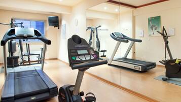 Un gimnasio con diverso equipo de ejercicio, incluyendo cintas de correr, elípticas y bicicletas estáticas.